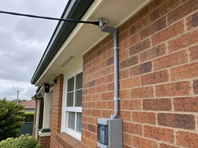 Overhead service cable and bracket on a brick house exterior beside a meter box in Kahibah