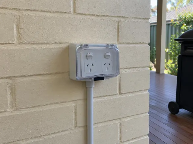 Outdoor double power point with weatherproof cover on a painted brick wall under a deck in Charlestown